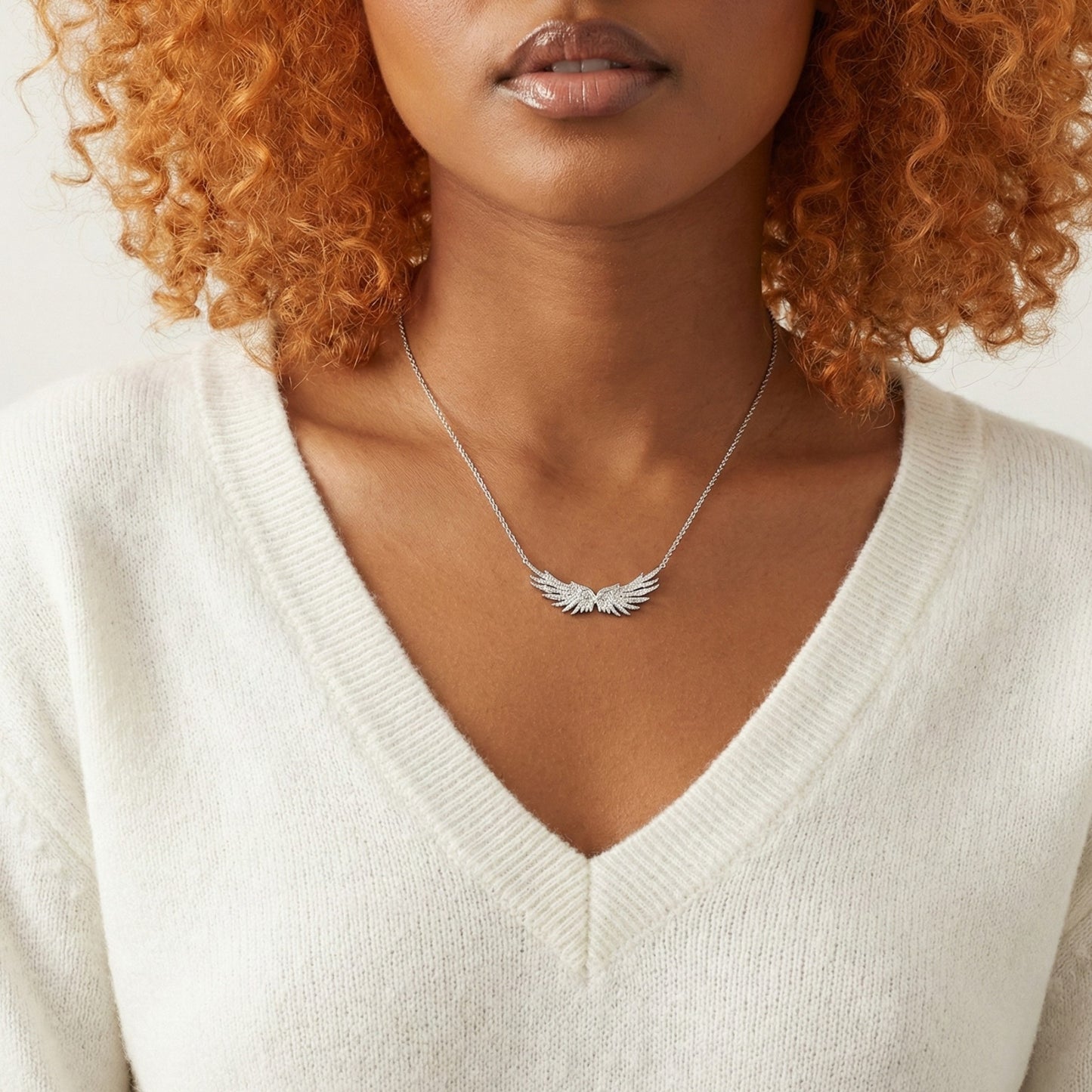 Woman wearing a silver necklace with an angel wing pendant against a neutral background