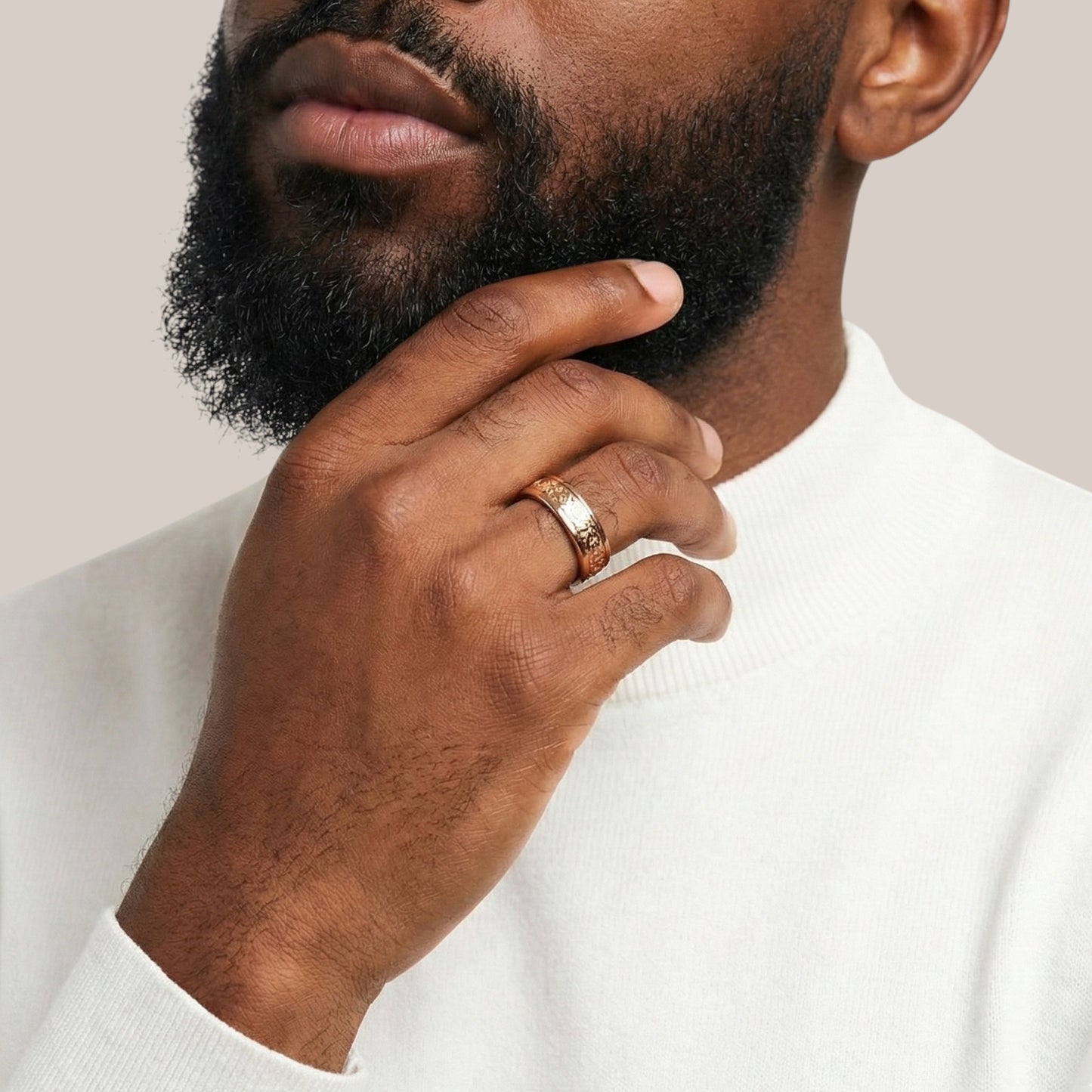 Man wearing a gold ring on his finger with a neutral background