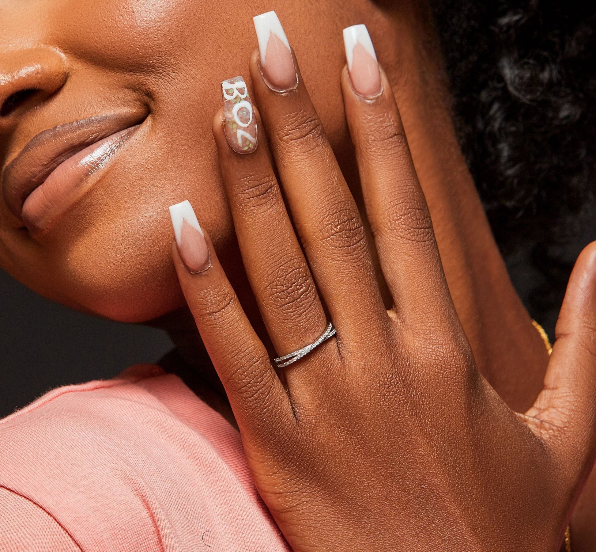 Close-up of a person with a ring on their finger and a visible brand logo on their nail.