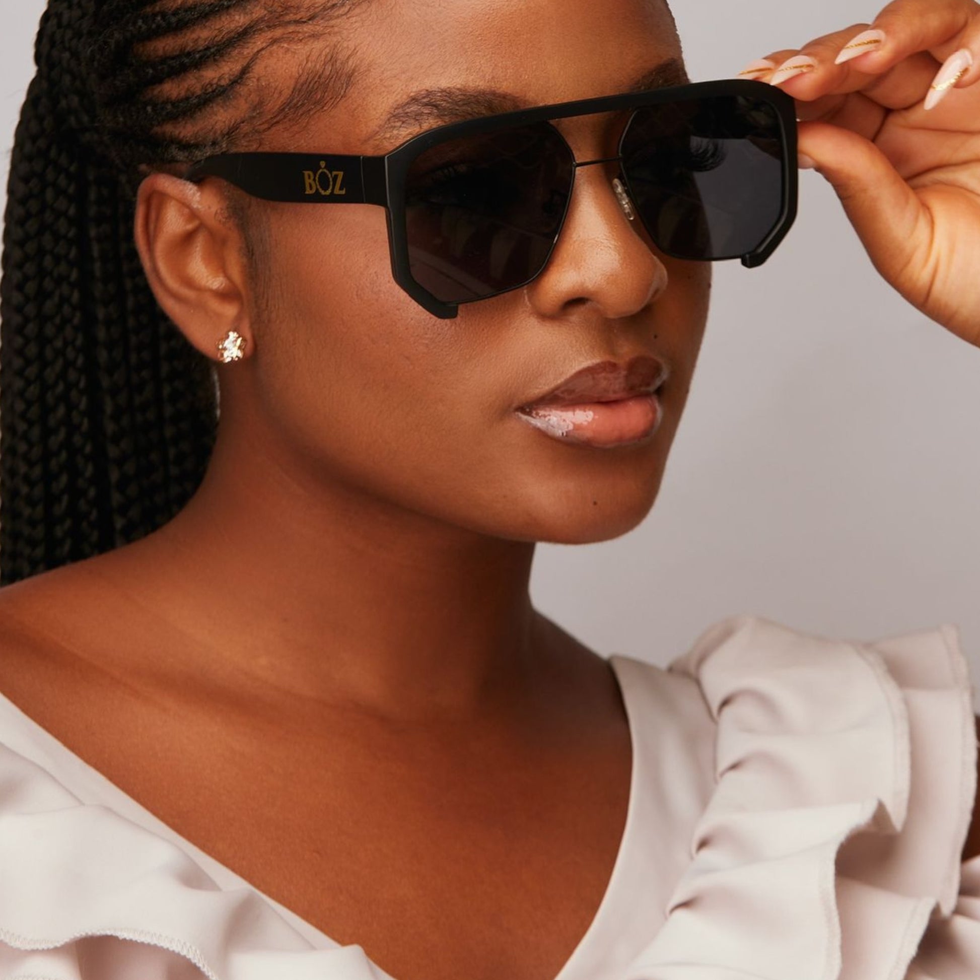 Woman wearing black sunglasses with 'BOZ' branding, holding them up to her face.