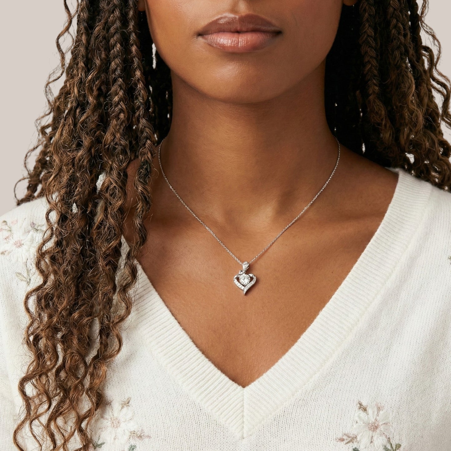 Woman wearing a silver necklace with a heart pendant against a neutral background