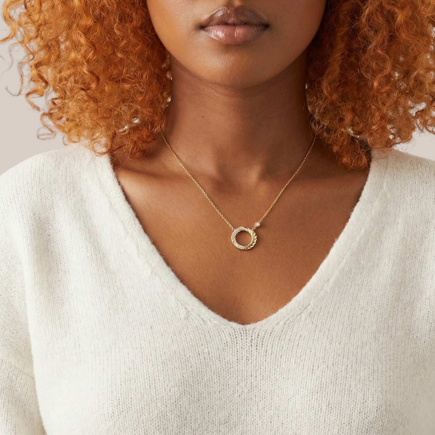Woman wearing a gold necklace with a circular pendant against a neutral background