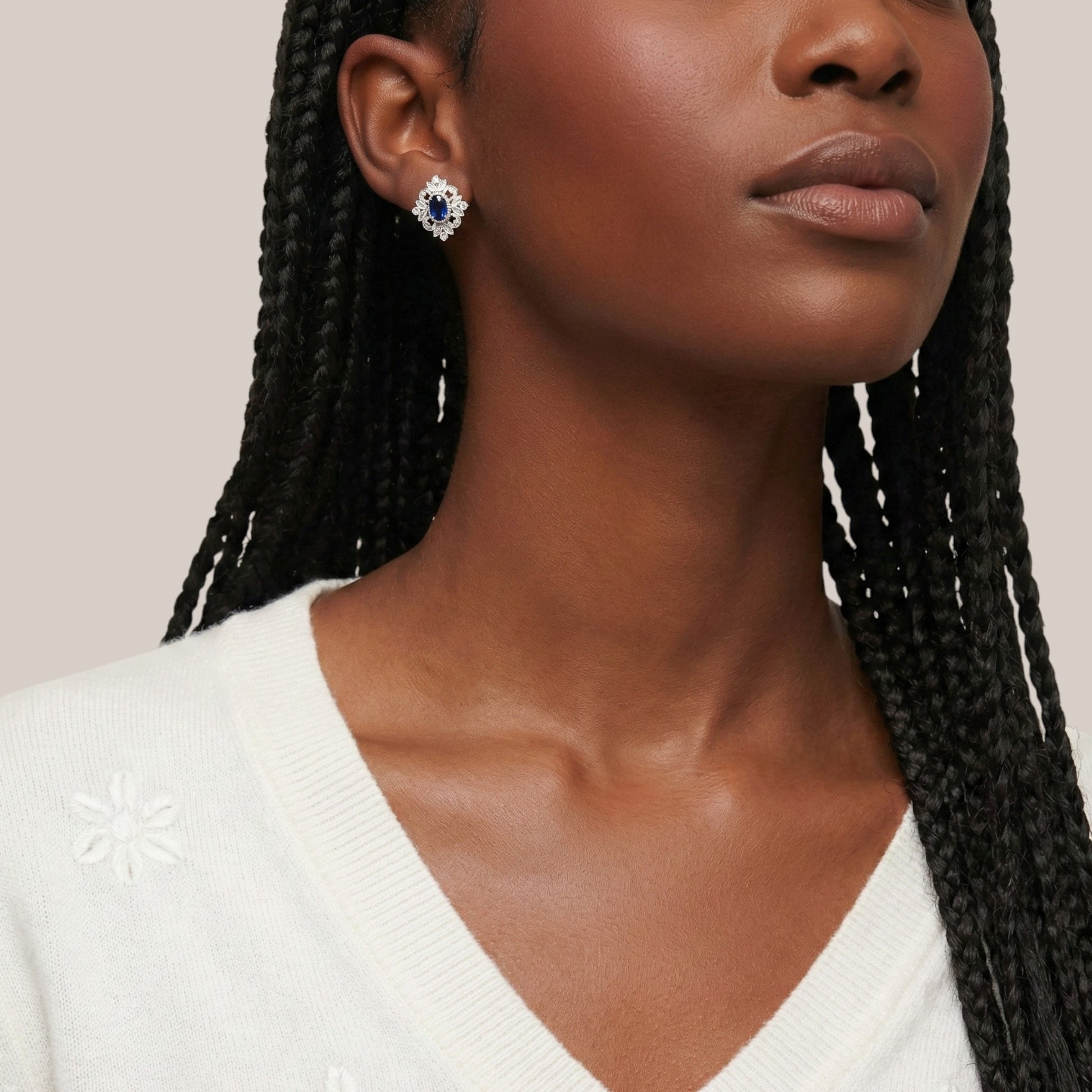 Woman wearing a pair of earrings with a white sweater on a neutral background