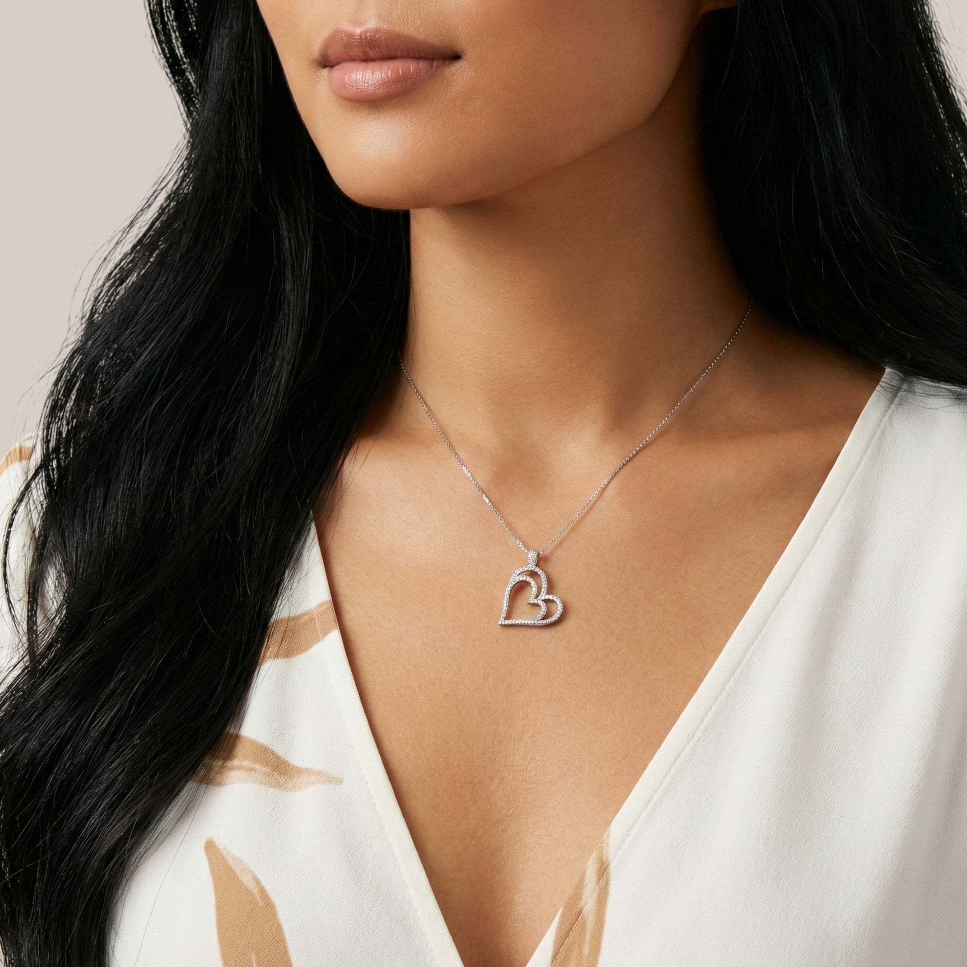 Woman wearing a silver necklace with a heart pendant against a neutral background