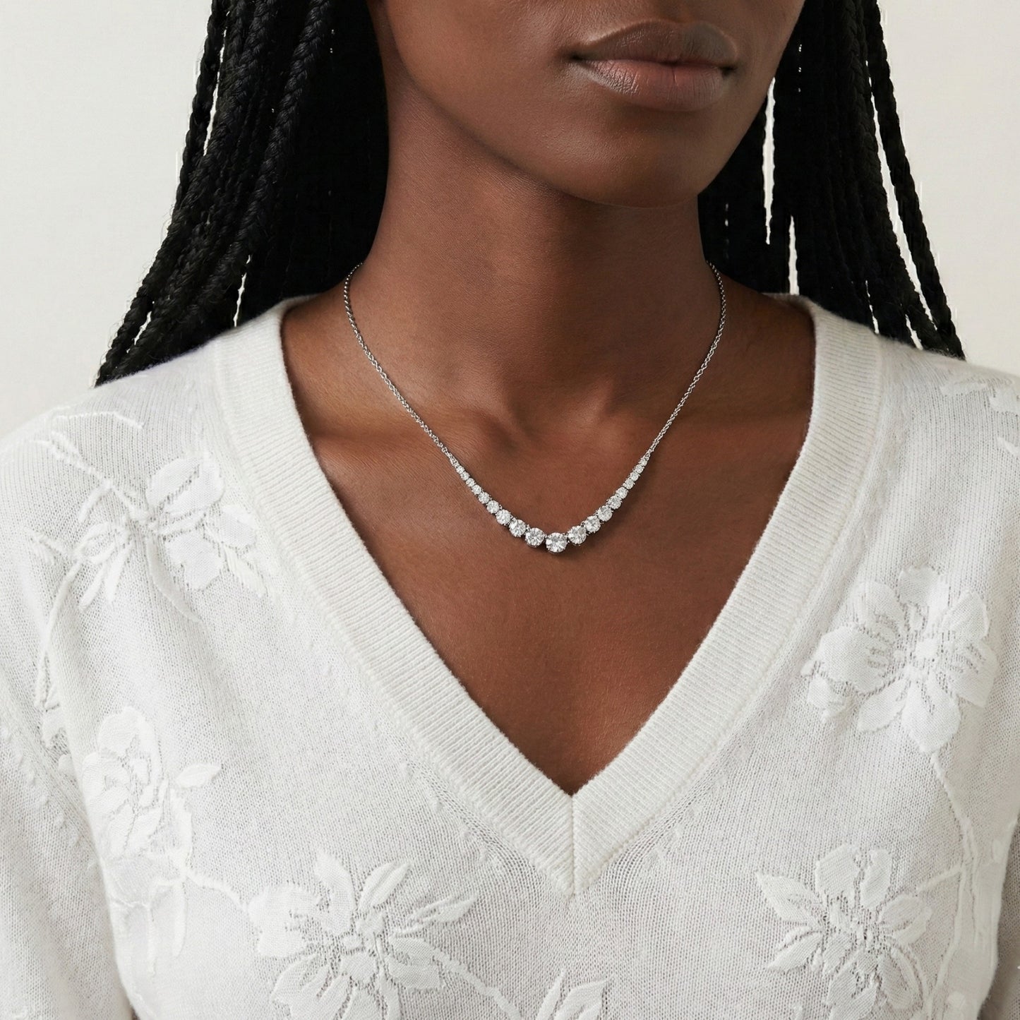 Woman wearing a silver necklace with a white embroidered top against a neutral background