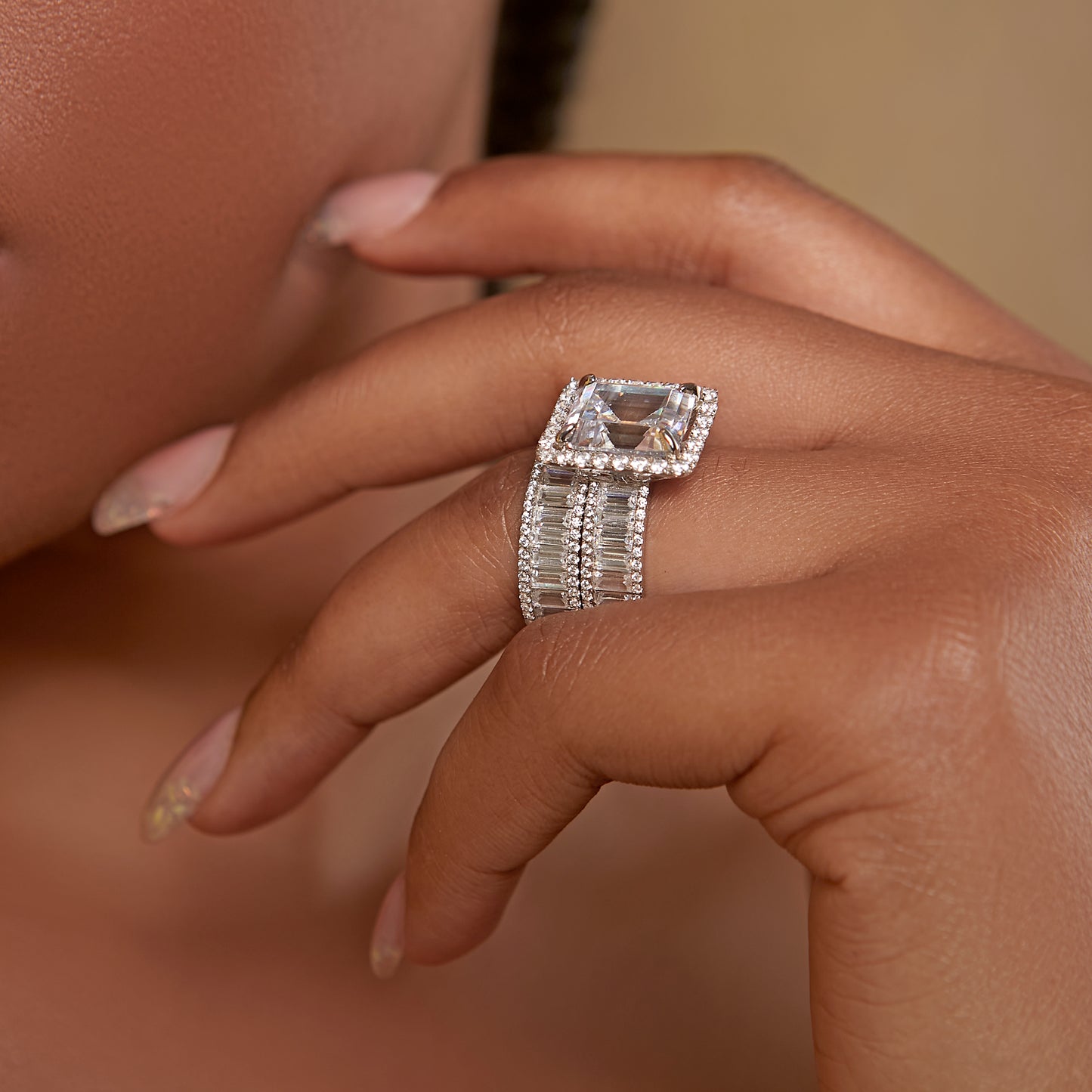 Close-up of a hand wearing a diamond ring with a beige background