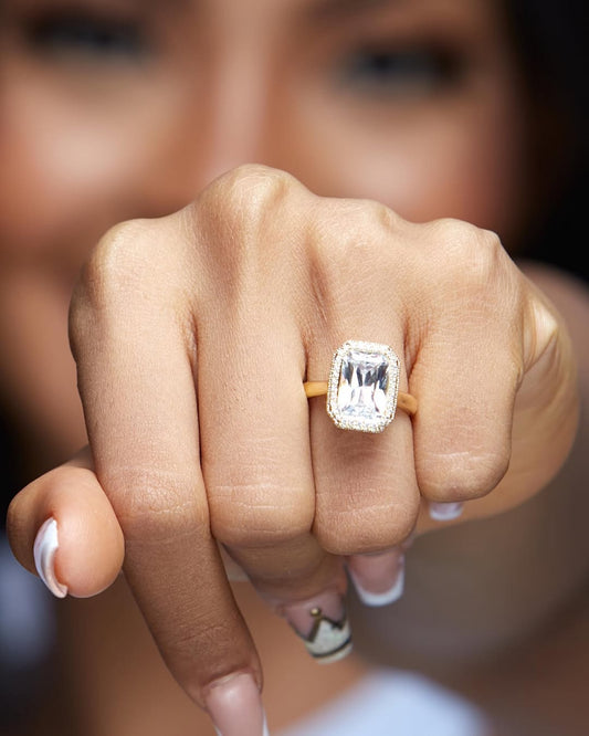 A person showcasing an 18K gold engagement ring with a moissanite center stone and diamond side stones.
